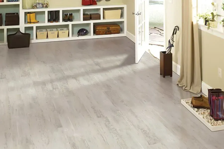 Light gray wood-look flooring in a room with built-in shelves, a door, and a pair of boots.