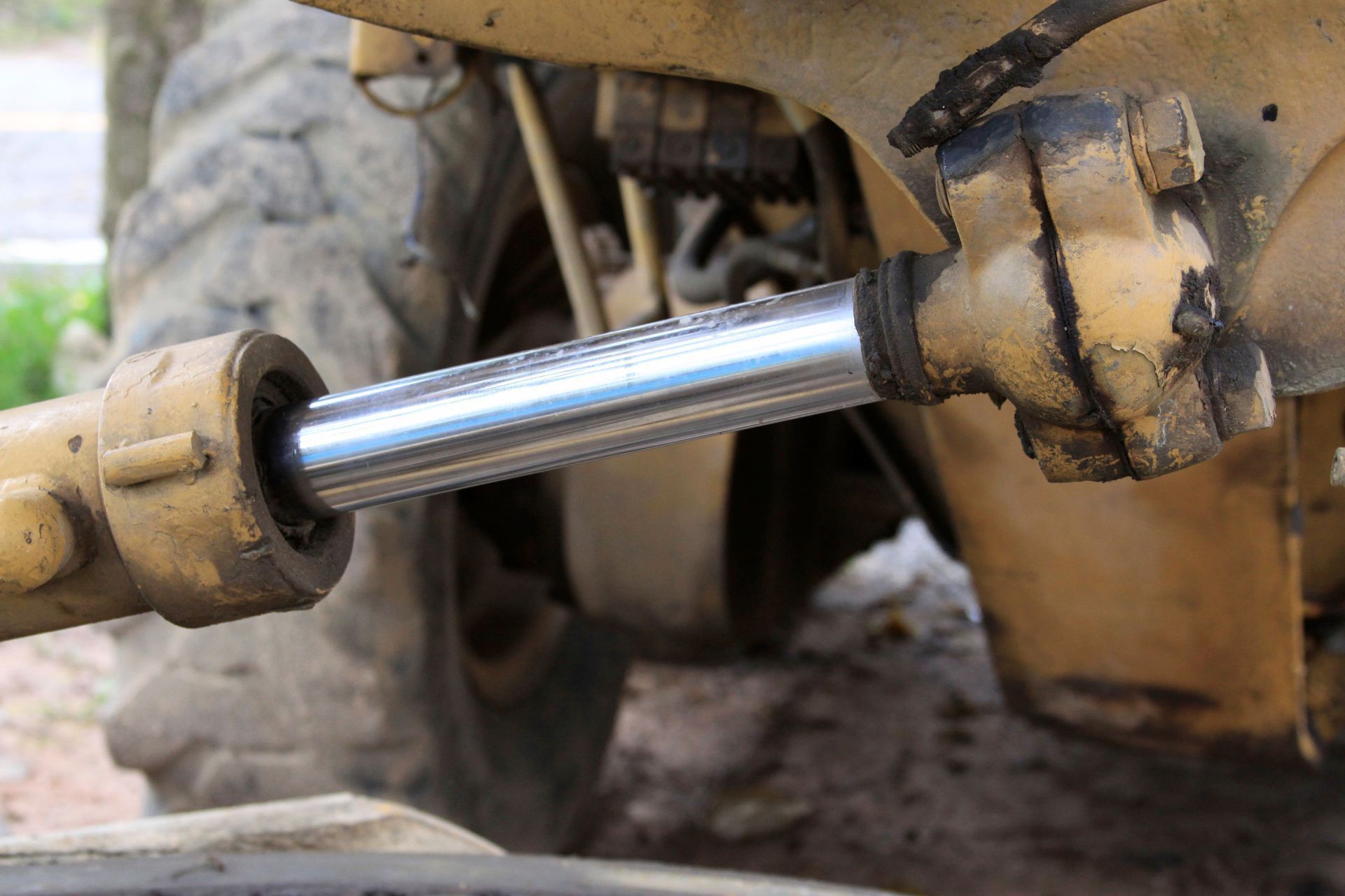 Close-up of a weathered yellow hydraulic cylinder piston extended from a construction vehicle.