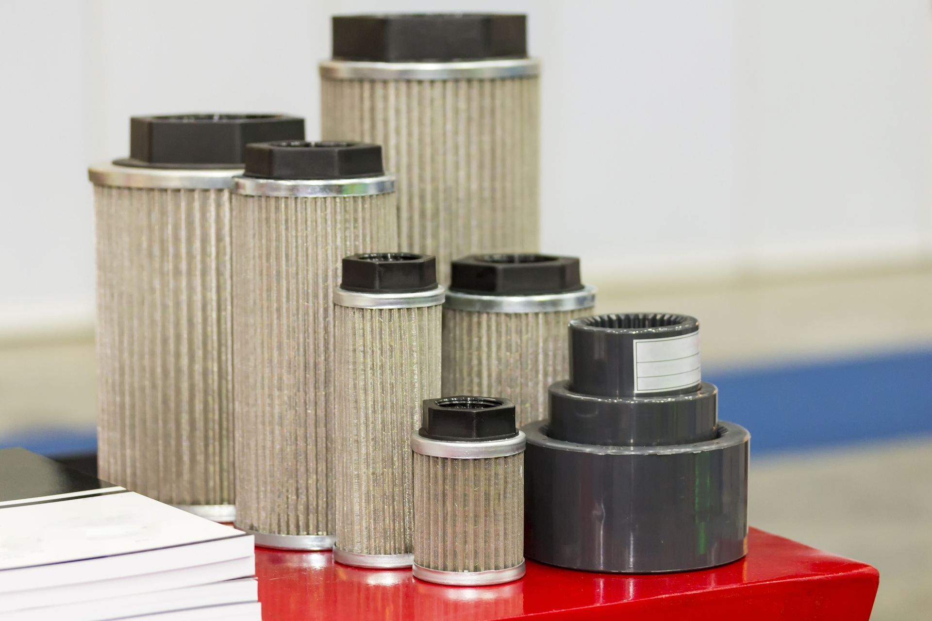 A collection of various sized cylindrical metal hydraulic filter elements standing on a red surface.