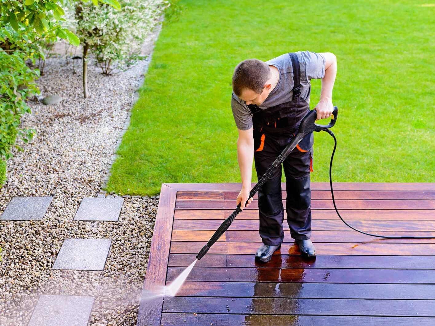 Man pressure washing a wooden deck, spraying water onto the planks.