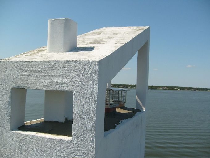 White concrete lookout structure on a pier over calm water under a clear blue sky