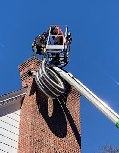 Worker in a lift installing coiled cable on top of a brick chimney against a blue sky