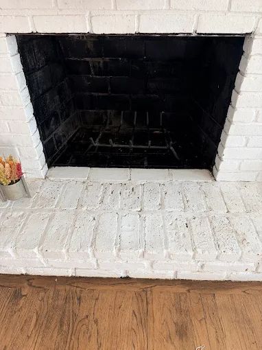 White painted brick fireplace with a black firebox and white hearth in a room with hardwood floor