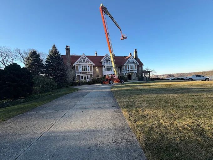 Large house with a red boom lift in the driveway under a clear blue sky