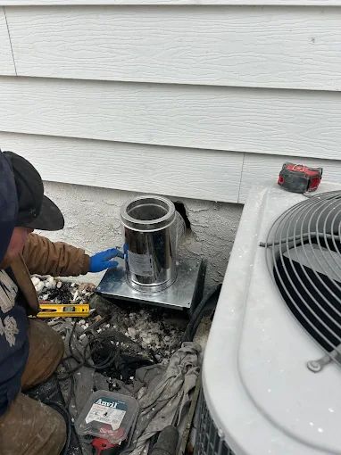 Technician working on a damaged metal vent unit beside an exterior wall and air conditioner.
