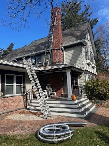 House porch with ladders leaning against the roof and a coiled hose on the brick patio.