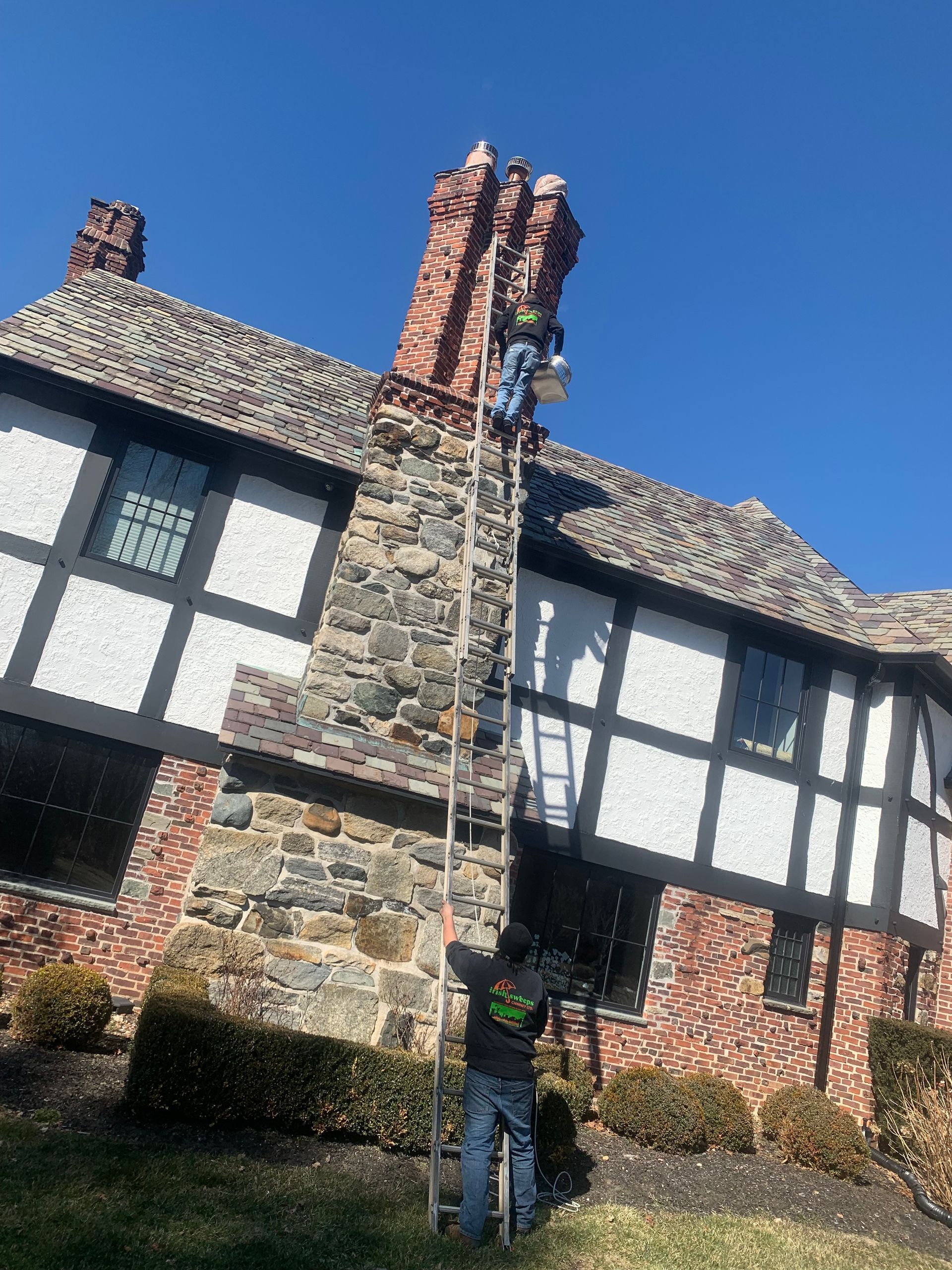Half-timbered house with stone chimney under a clear blue sky, viewed from below
