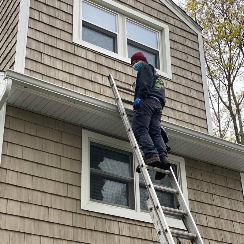 Person on a ladder cleaning or working on the roof of a house