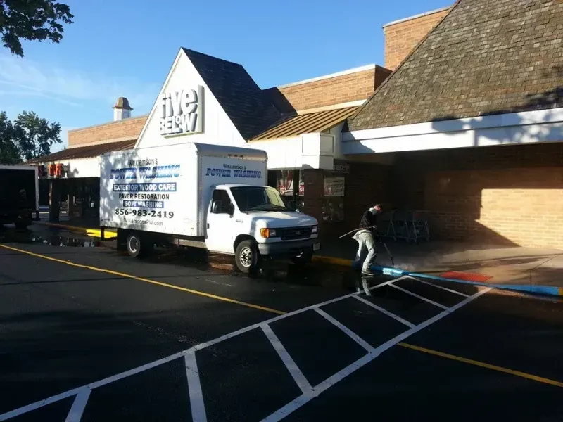 White truck parked in front of a Five Below store; person sprays the crosswalk with water.