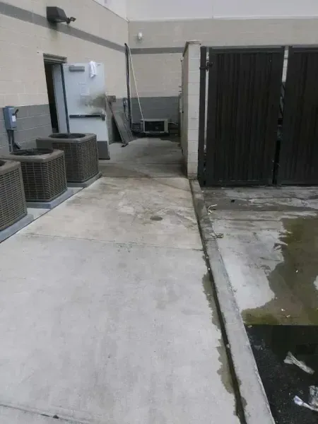 Concrete walkway with air conditioning units, open doorway, and gate; appears wet.