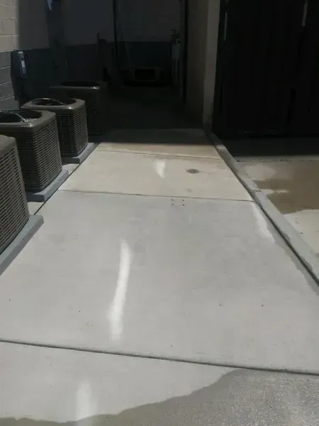 Concrete walkway with AC units on the left and a dark doorway on the right.