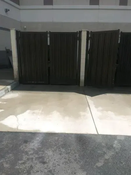 Wooden gate with concrete path. Dark brown gate panels, white columns. Sunny outdoor setting.