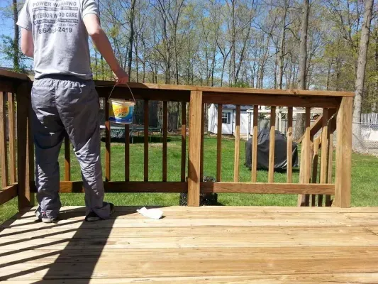 Person staining a wooden deck railing outdoors on a sunny day.