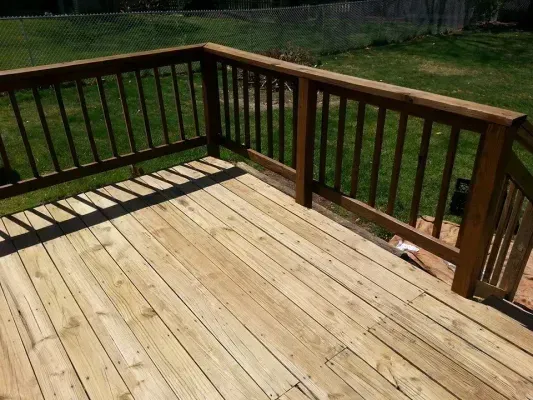 Wooden deck with brown railing, casting shadows on the light-colored planks; green grass in background.