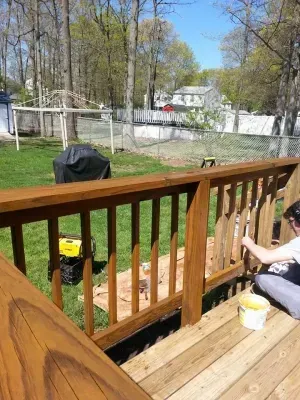 Person staining wooden deck railing outdoors on a sunny day.