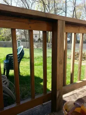 Wooden deck railing overlooking a grassy yard with a green chair.
