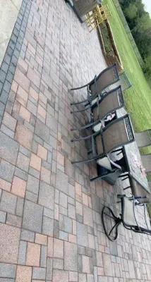 Patio with brick pavers, metal chairs, and a table beside a grassy lawn.