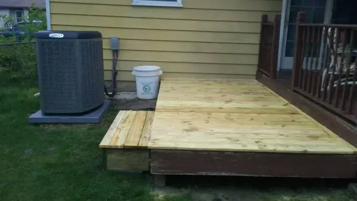 Wooden deck and steps next to a house with an air conditioning unit on the grass.