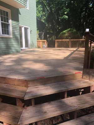 Wooden deck outside a light green house with stairs leading down.