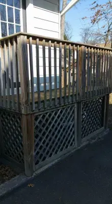 Wooden deck with lattice skirting, attached to a white building; weathered wood and asphalt.
