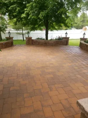 Brick patio with low brick walls, lampposts, and a large tree in a yard.