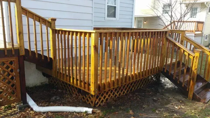 Wooden deck with railing and stairs, attached to a house with a white downspout.
