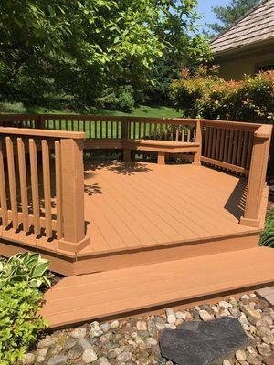 Wooden deck with built-in seating, surrounded by railing. Browns and greens in a garden setting.