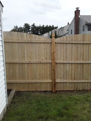 Wooden fence with a gate in a grassy backyard, cloudy sky in the background.