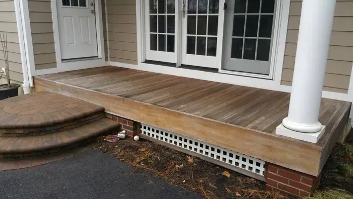 Wooden porch with brick base and steps. Door and column present.