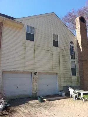 Yellow-sided house with green algae streaks, two garage doors, and a brick chimney.