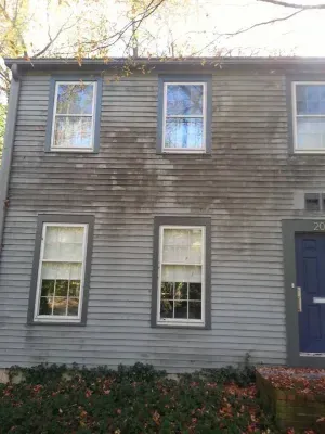 Two-story gray house with weathered siding, four windows, and a blue front door.