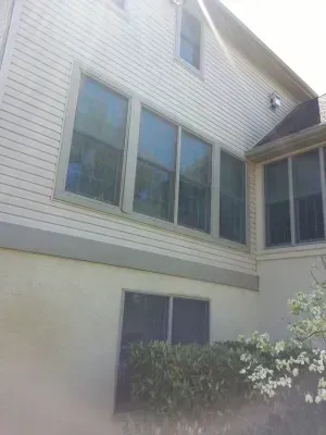 Exterior of a house with light siding and multiple windows; greenery visible.