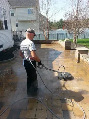 Man pressure washing a brick patio.