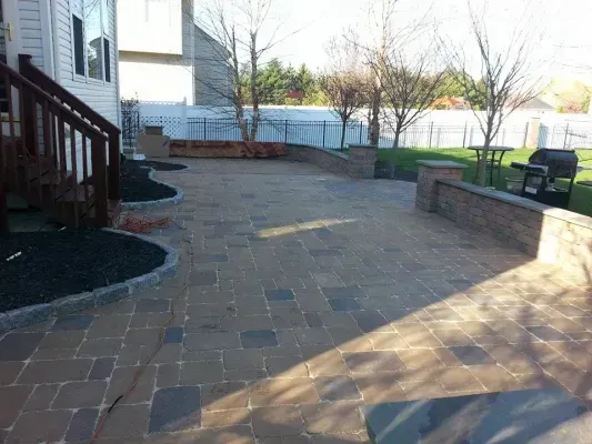 Brick patio with low walls and wooden deck. Lawn and trees in background, sunny day.
