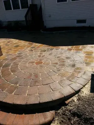 Circular brick patio with surrounding pathway next to a white house.