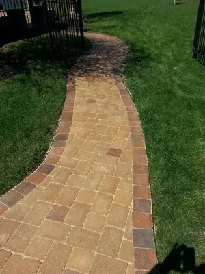 Brick pathway with brown and tan pavers, bordered by reddish-brown bricks, winding through green grass.