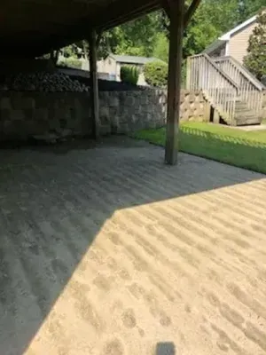 A covered concrete patio with visible ridges. A retaining wall and stairs lead up to a grassy area and house.