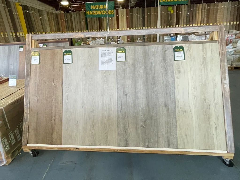 A display rack in a flooring store showcasing various wood-look planks in light to medium brown and grey tones.