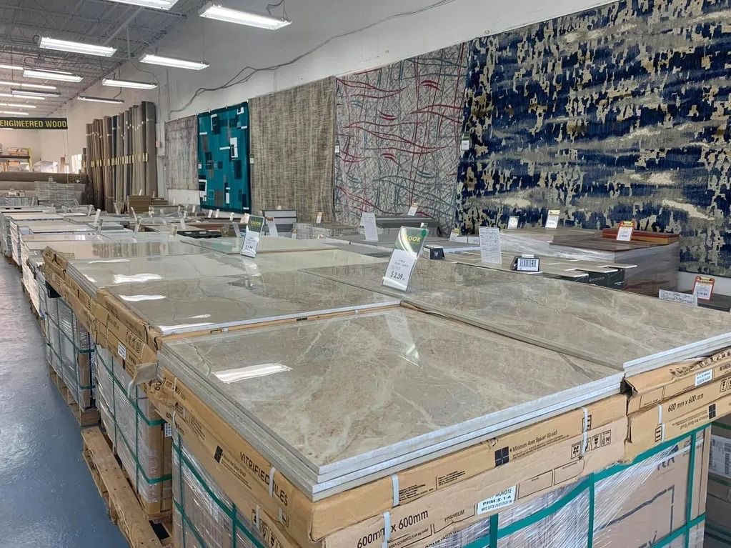 Pallets of stacked beige tiles in a store with area rugs hanging on the wall.