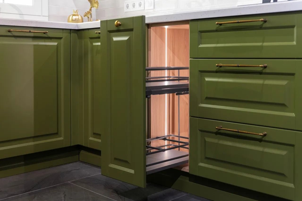 Olive green kitchen cabinets with brass handles, featuring a narrow pull-out spice rack drawer partially open.