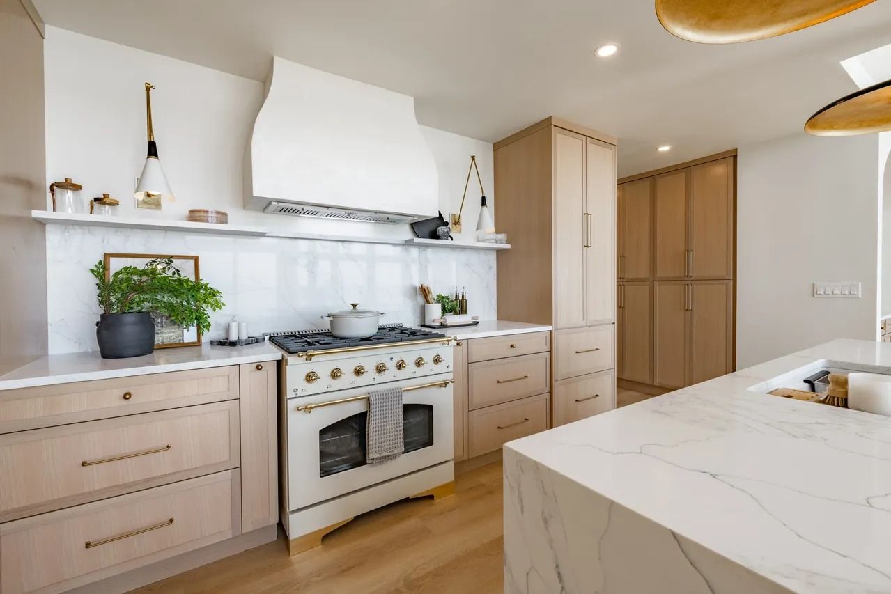 Modern kitchen with light wood cabinets, white range and hood, marble countertops, and a kitchen island.