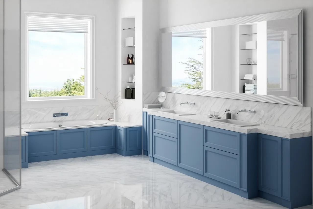 Bright, modern bathroom with blue cabinetry, white marble countertops, a large mirror, and a window above a bathtub.