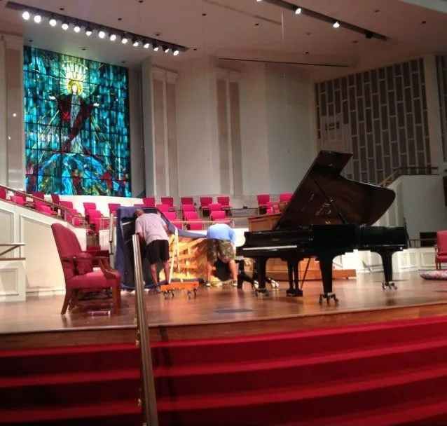 A group of people are working on a piano in a church