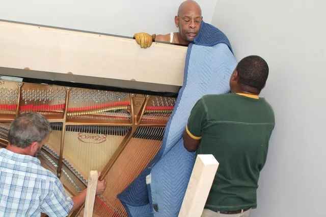 Three men are moving a piano up a staircase.