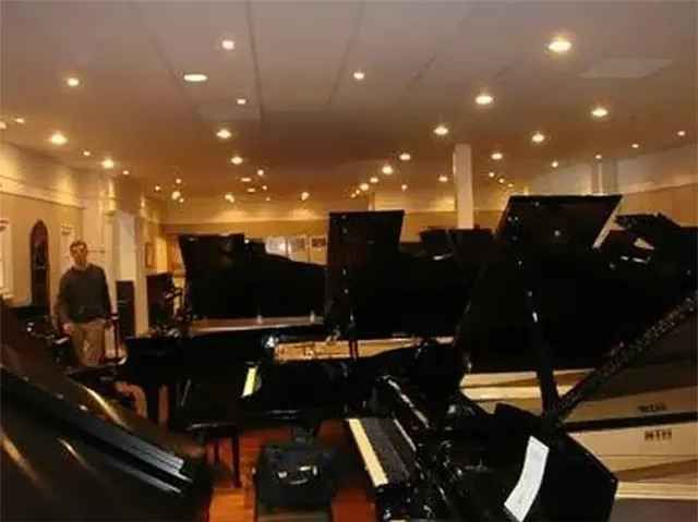 A man is standing in a room full of pianos