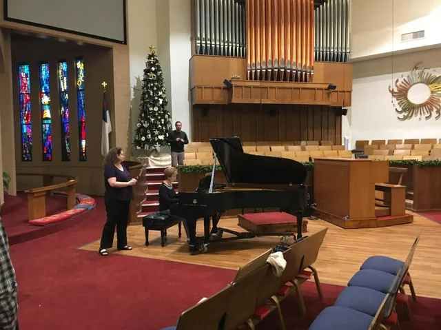 A woman is playing a piano in a church with a christmas tree in the background.
