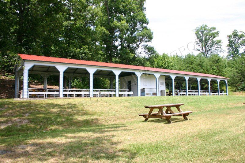 A long pavilion with a red roof and a picnic table in front of it