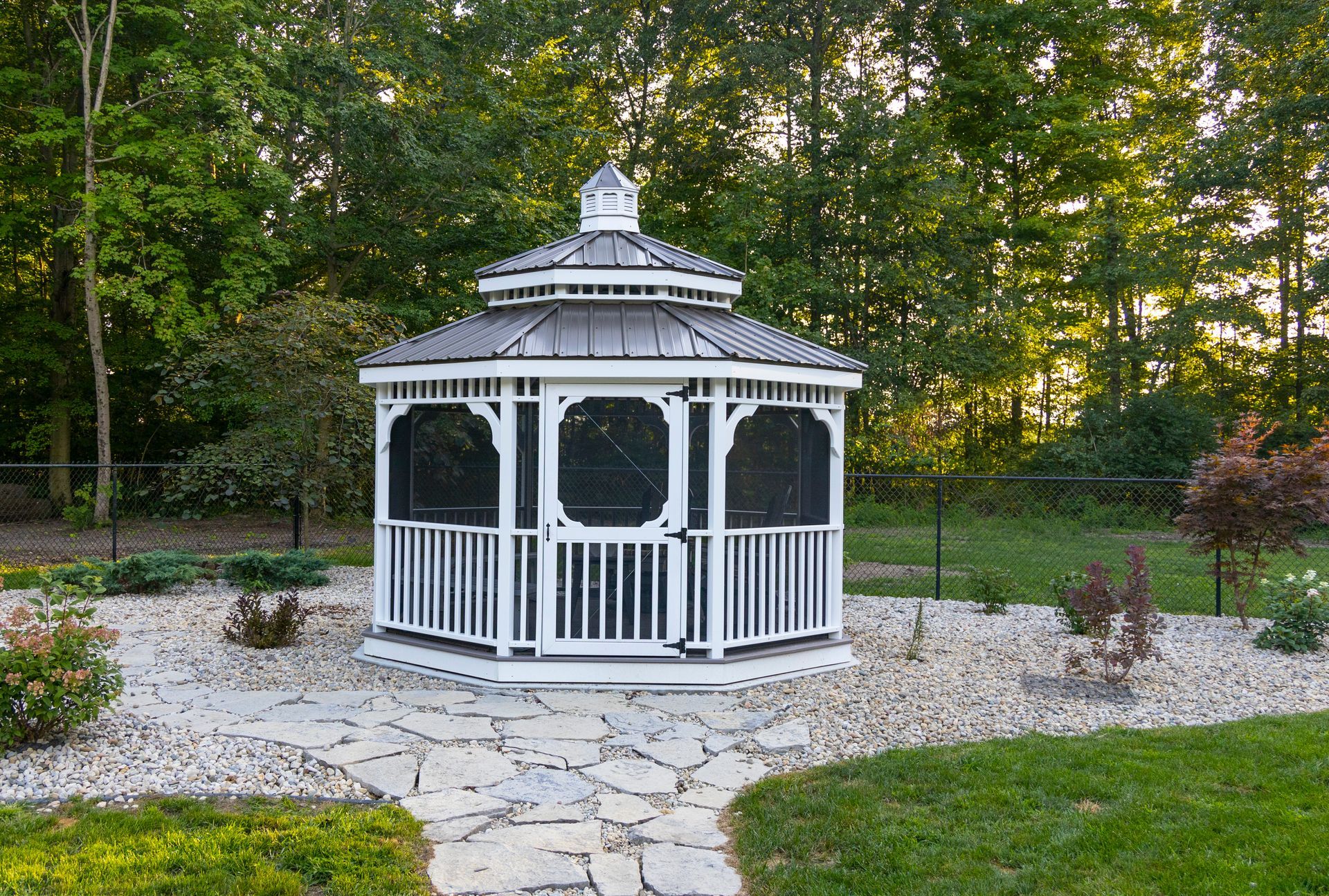 A white gazebo with a screened in porch in a backyard surrounded by trees.
