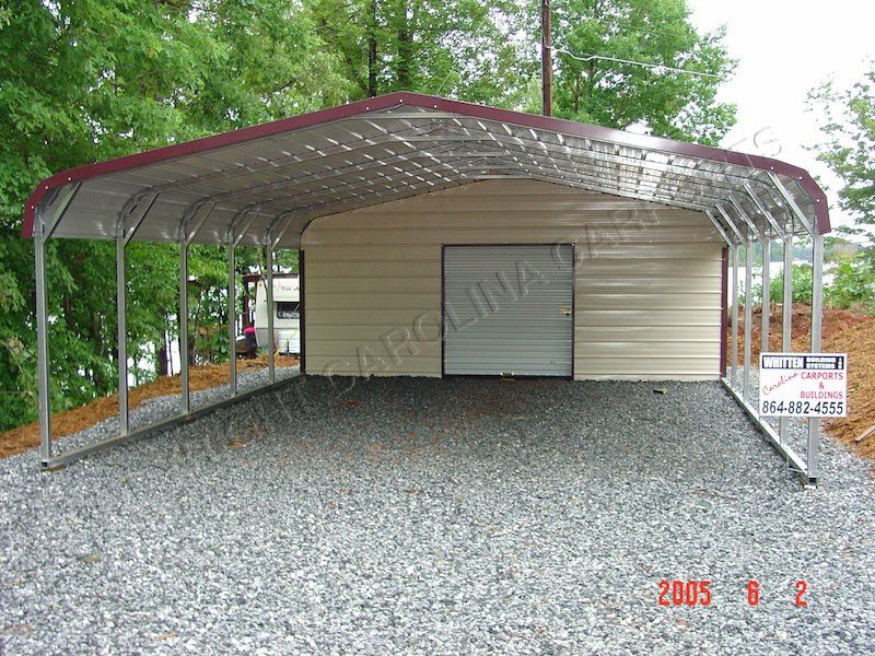 A carport with a red roof is sitting on gravel.