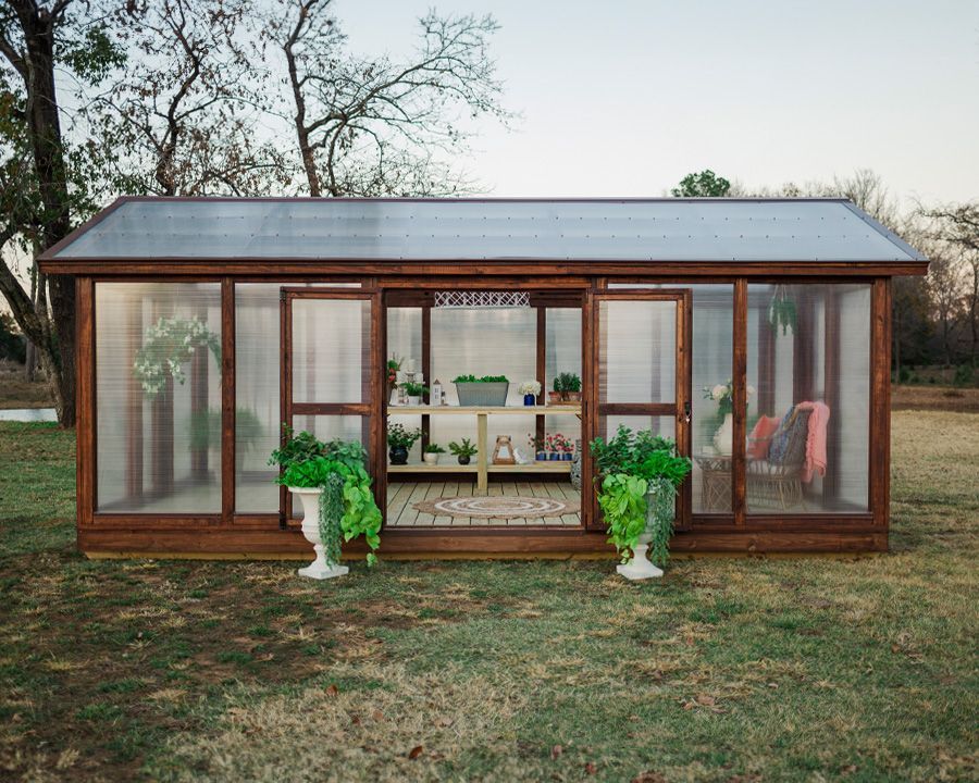 Greenhouse with open doors, plants, and interior decor, set in an outdoor grassy area